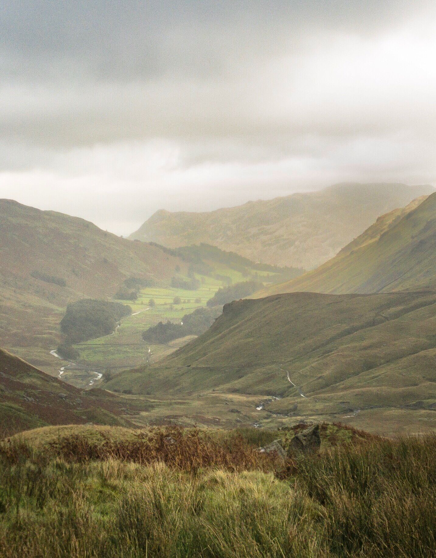 A valley with a river, rolling hills, and a cloudy sky.