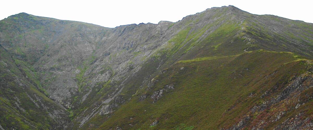 A rugged mountain with steep slopes and patches of green vegetation.