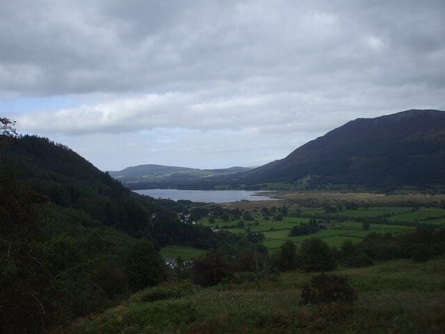 A valley with a lake, surrounded by hills and green fields.