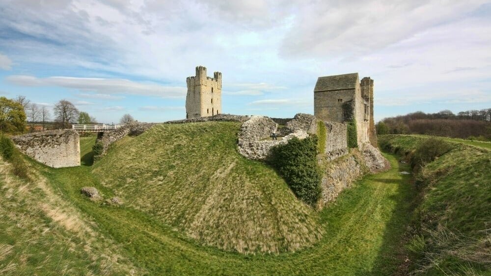 A historic castle ruin with two towers on a grassy hill.