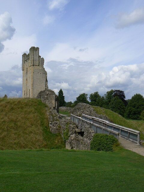 A ruined castle on a grassy hill with a metal bridge leading to it.