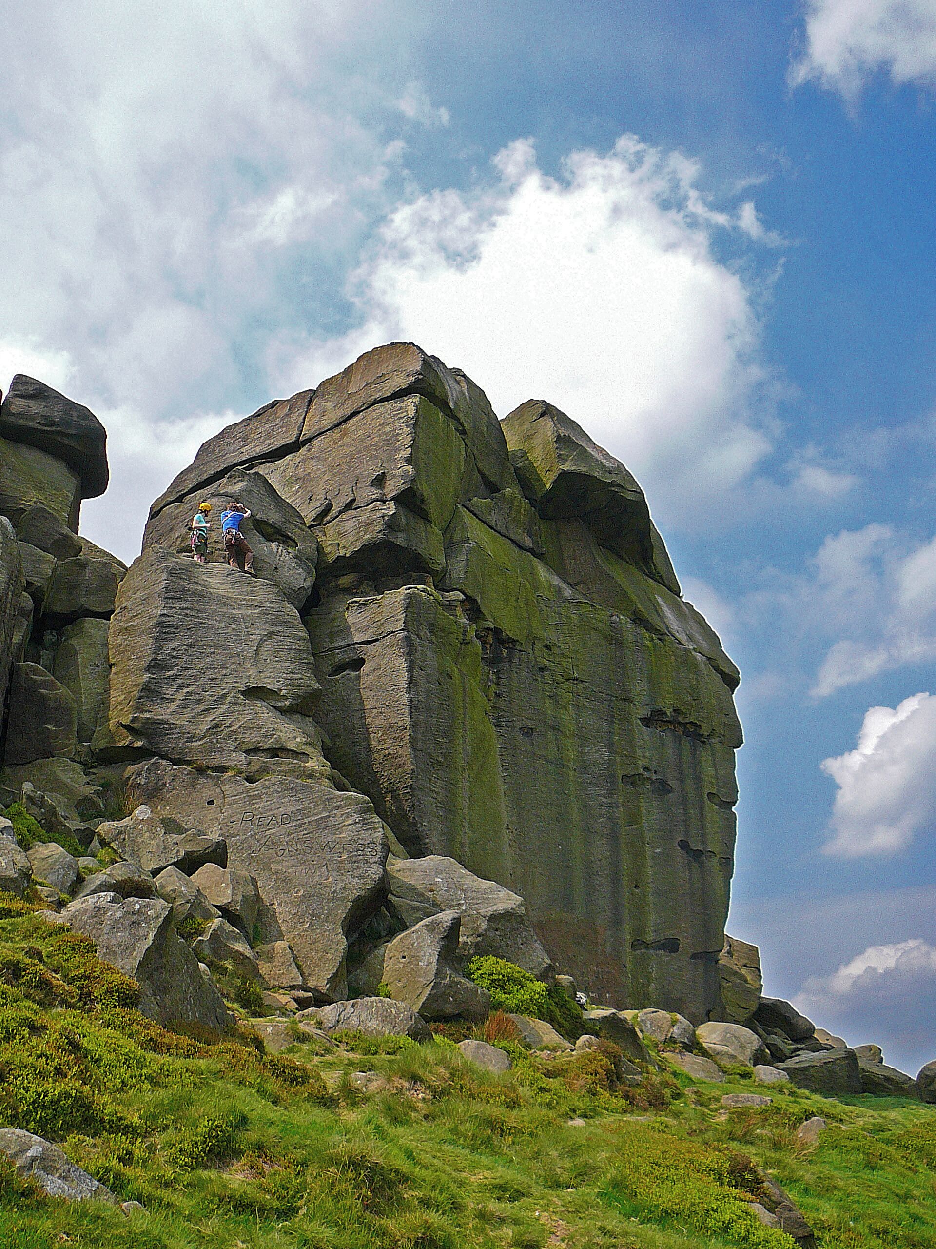A large rock formation with two hikers climbing.