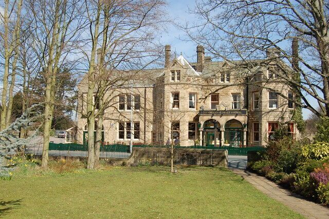 A large, historic stone building with a green entrance and a well-maintained lawn in front.
