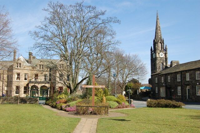 A historic building with a clock tower, surrounded by a well-maintained garden and a clear sky.