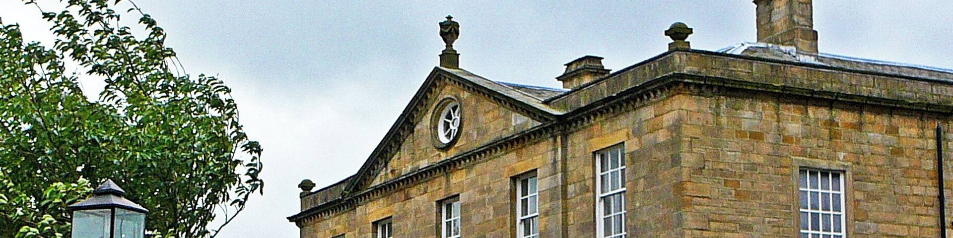 A historic stone building with a clock tower, ivy-covered walls, and a gated entrance.