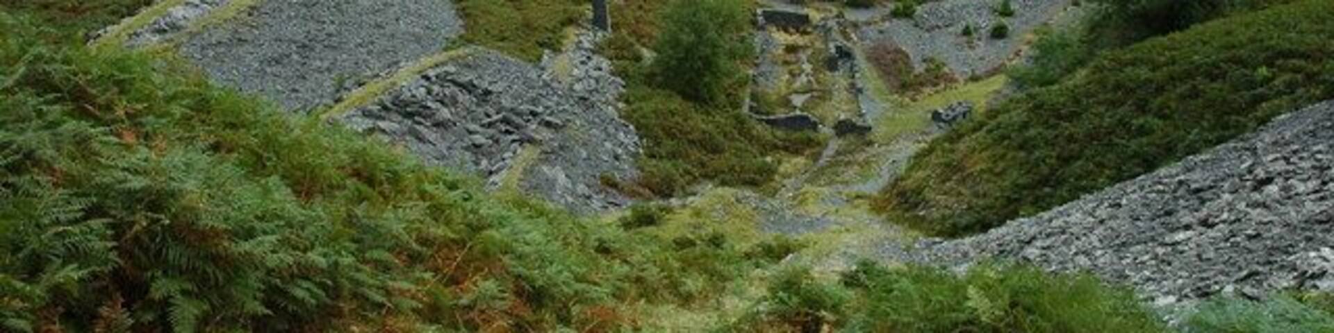 A mountainous landscape with a ruined stone structure surrounded by greenery and a valley.