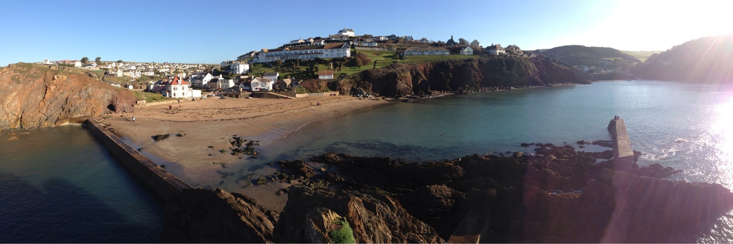 A coastal town with a prominent hilltop house, sandy beach, rocky shoreline, and calm sea.