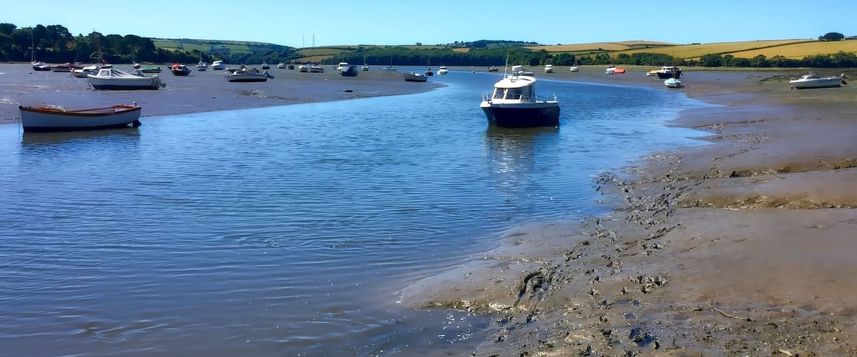 A calm river with boats, a sandy shore, and green hills in the background.