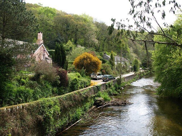A river flowing through a lush, green landscape with a small house and a bridge.