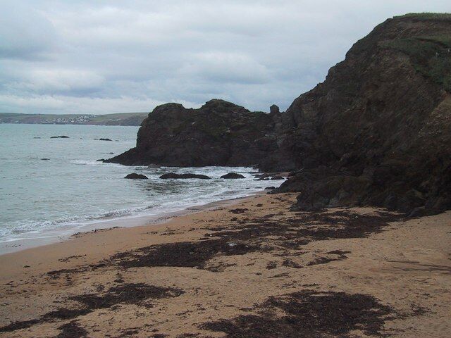 Costa rochosa com uma praia de areia e céu nublado.