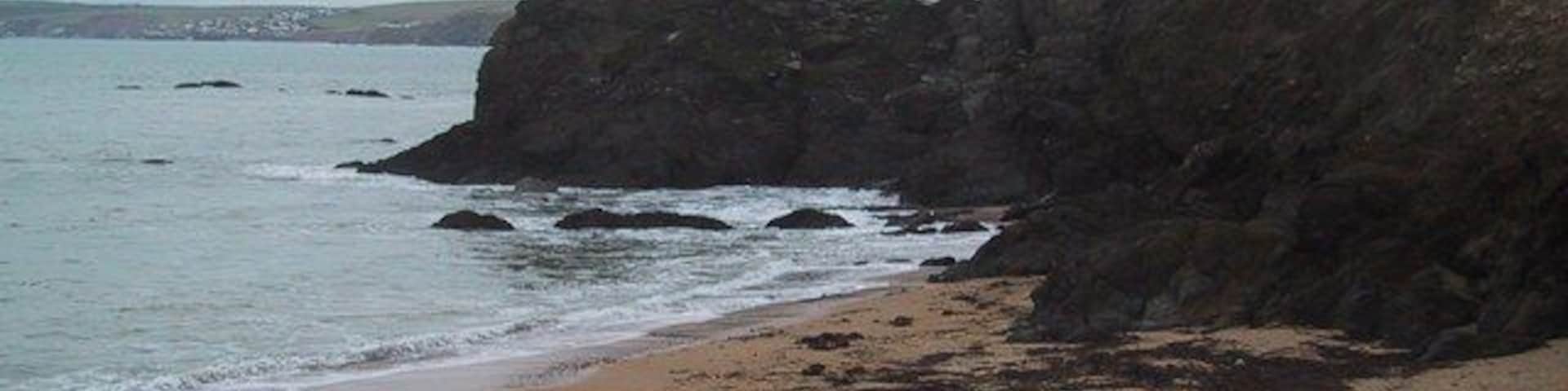 Costa rochosa com uma praia de areia e céu nublado.