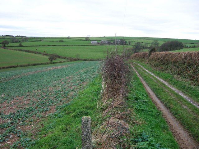 A rural landscape with fields, a dirt path, and a stone wall.