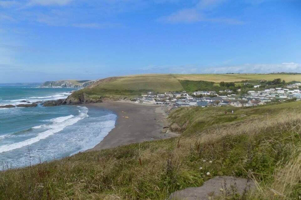 Un pueblo costero con playa, colinas cubiertas de hierba y acantilados.