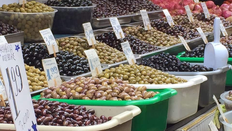A market with various fruits and vegetables displayed in bins, including cherries, strawberries, and olives.