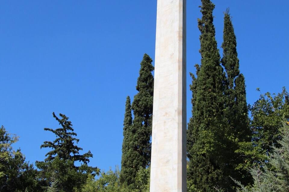 A tall monument with a statue of a warrior at the top, a statue of a dog, and a person standing in front.