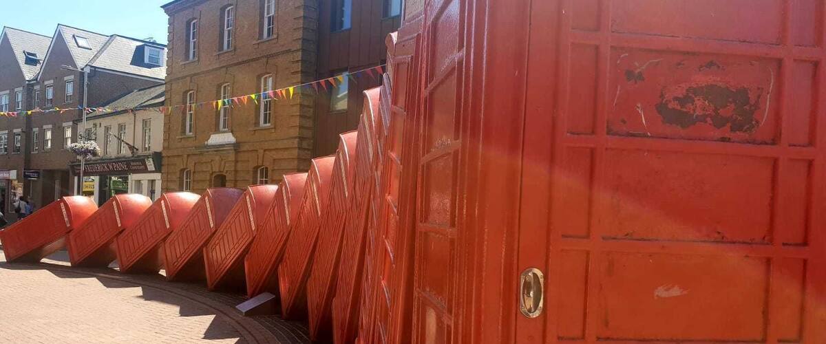 A row of red doors in a public square with brick pavement and buildings in the background.