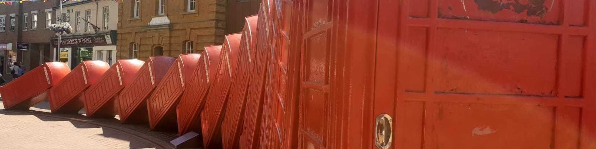 Uma fileira de portas vermelhas em uma praça pública com calçamento de tijolos e edifícios ao fundo.