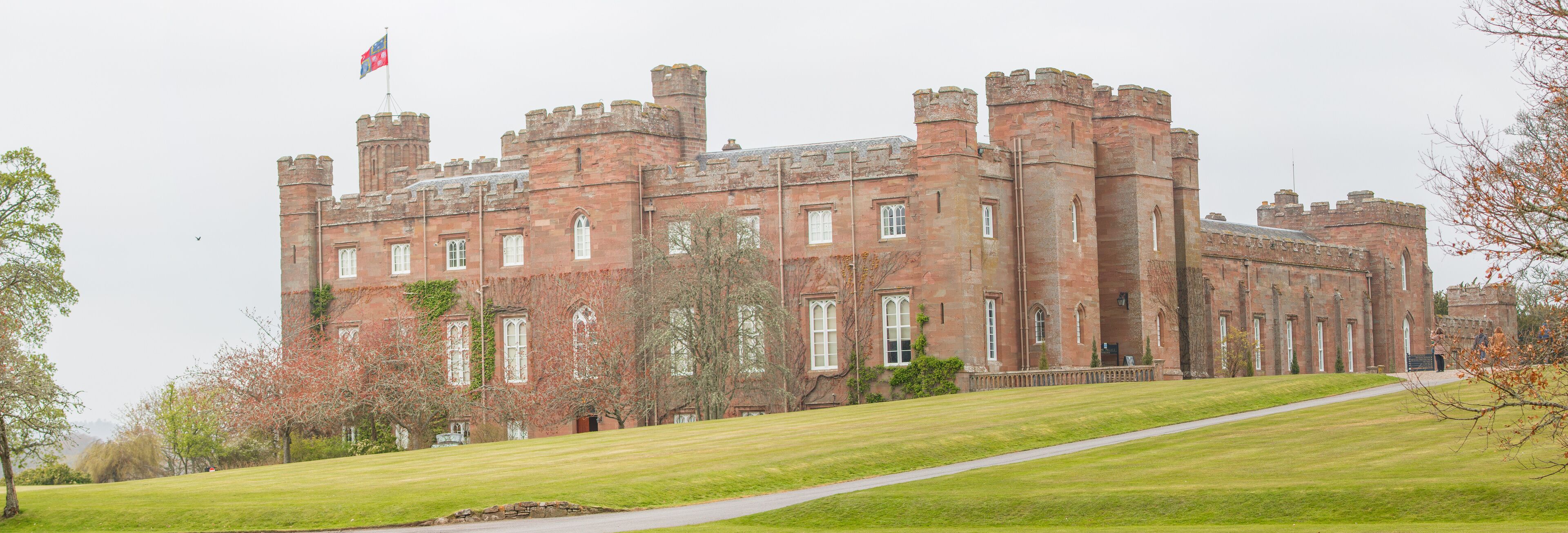 A large, historic castle with red brick walls, multiple towers, and a flag on top.