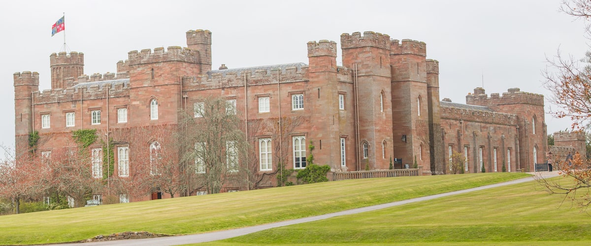 A large, historic castle with red brick walls, multiple towers, and a flag on top.