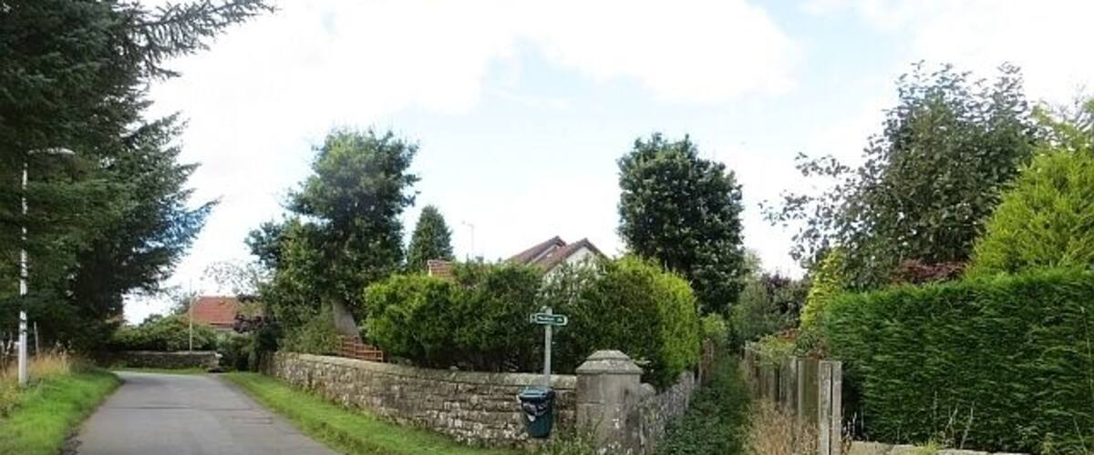 A narrow rural road flanked by stone walls and lush greenery.