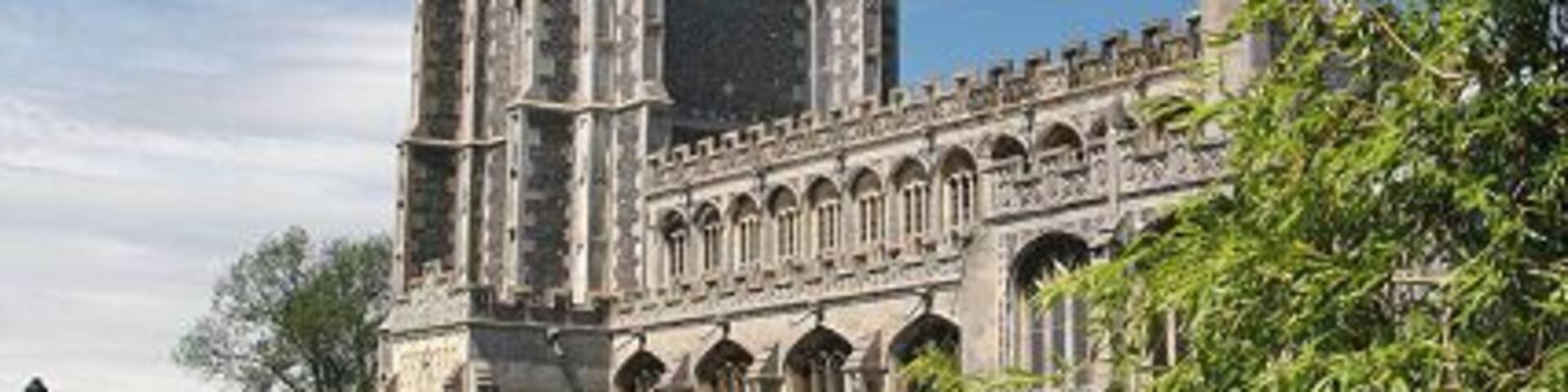 A historic cathedral with a tall tower and a spire, surrounded by lush greenery.
