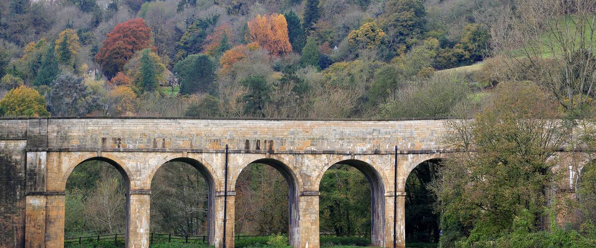 A stone viaduct with multiple arches over a green field.