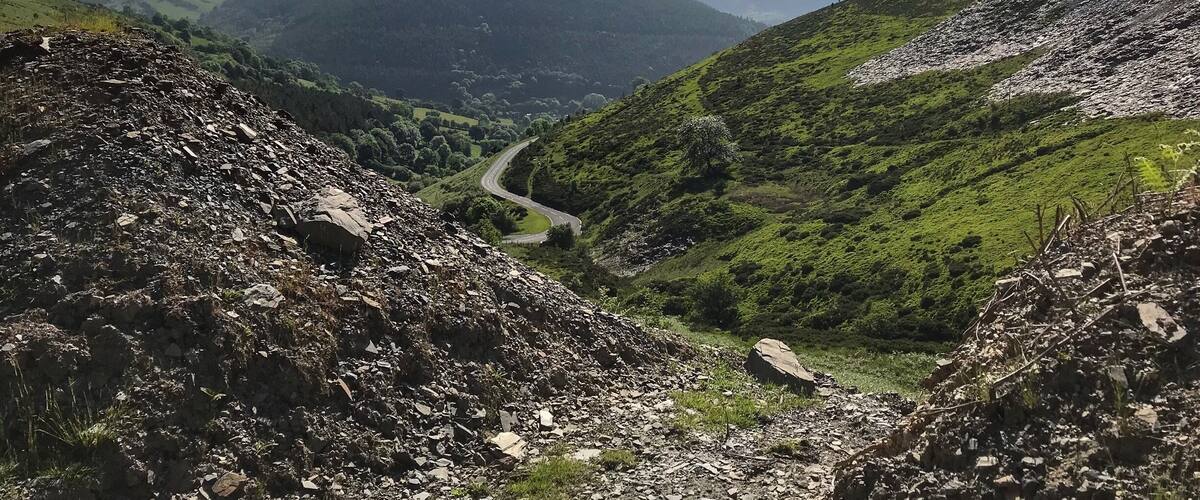 Een kronkelende bergweg door een vallei met rotsachtig terrein en glooiende groene heuvels.