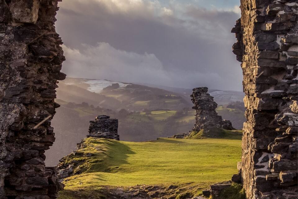 A stone archway framing a grassy landscape with distant hills and ruins.
