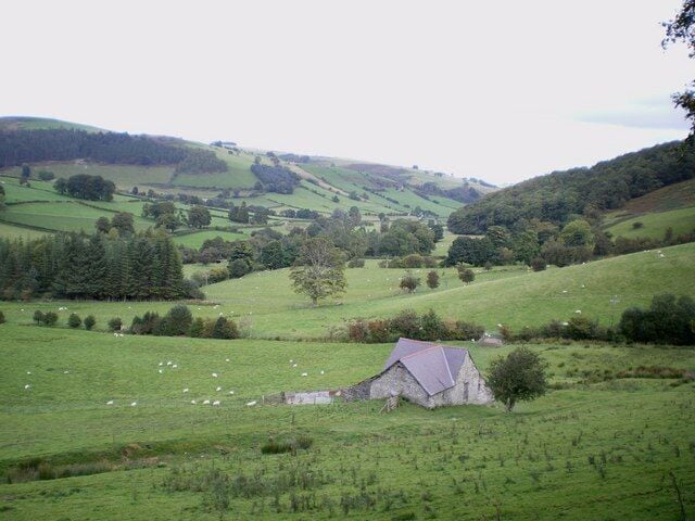 A rural landscape with rolling hills, a stone house, and grazing sheep.
