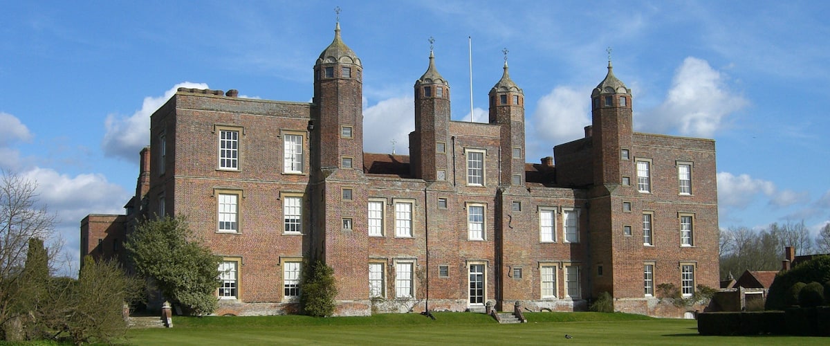 A large brick building with multiple towers and a well-maintained lawn.