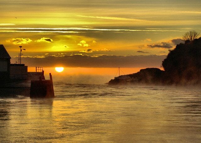 Atardecer sobre una zona costera con muelle y acantilados rocosos.