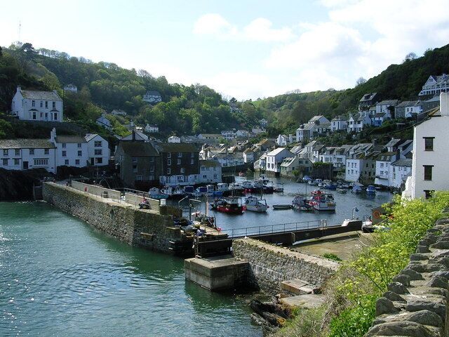 A coastal town with white buildings, a stone wall, and boats docked in the harbor.