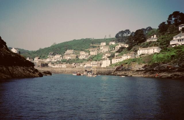 A coastal town with buildings on a hillside, a calm sea, and a rocky shoreline.