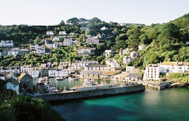 A coastal town with houses on a hillside, a harbor with boats, and a clear blue sea.