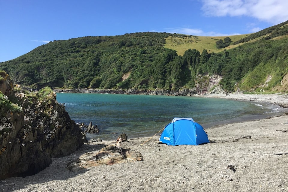 A beach with a tent and rocky cliffs.
