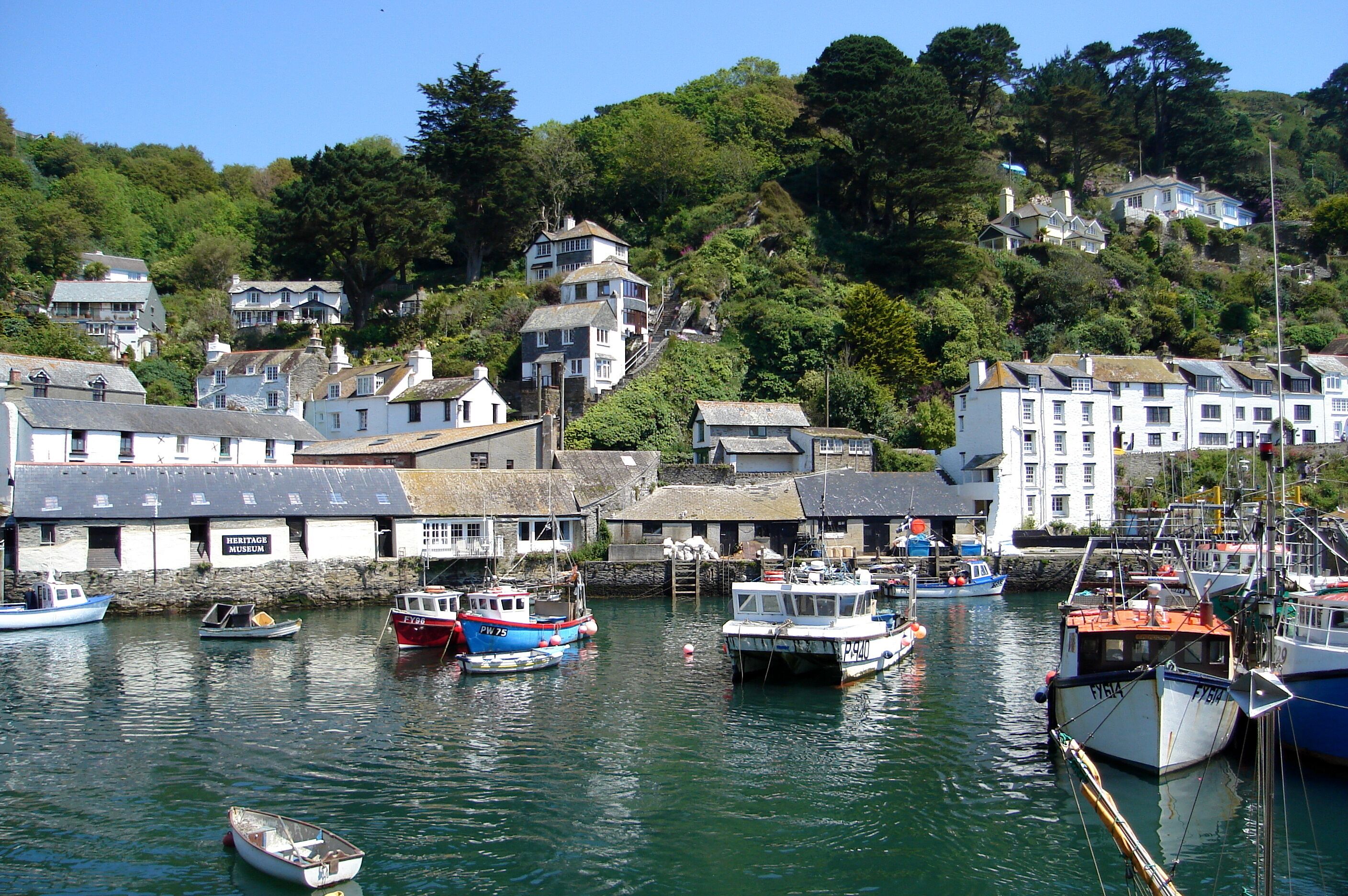 A harbor with boats docked, a Heritage Museum, and houses on a hillside.