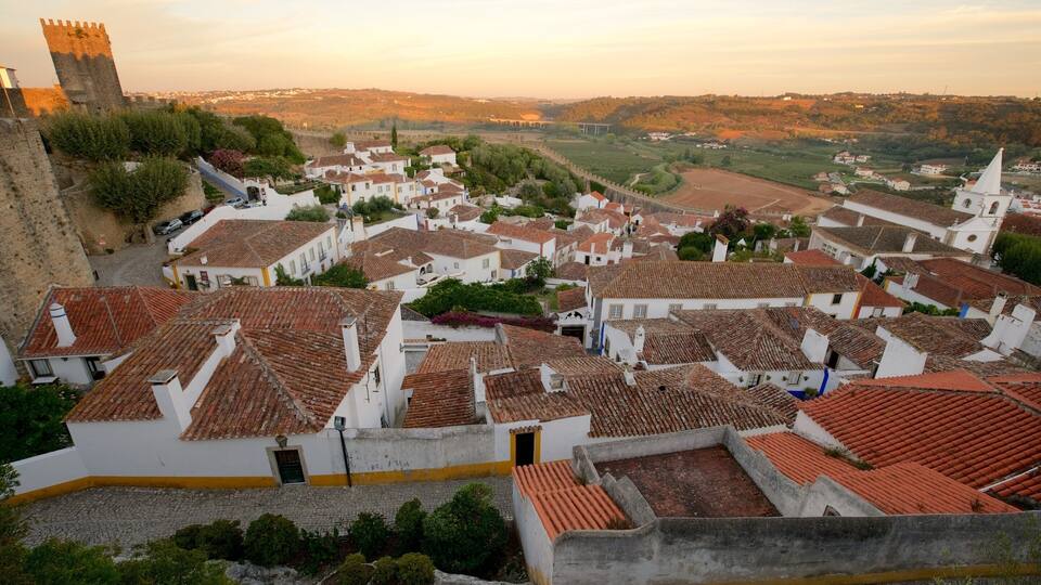 A historic town with white buildings and red-tiled roofs, surrounded by a stone wall and a tower.