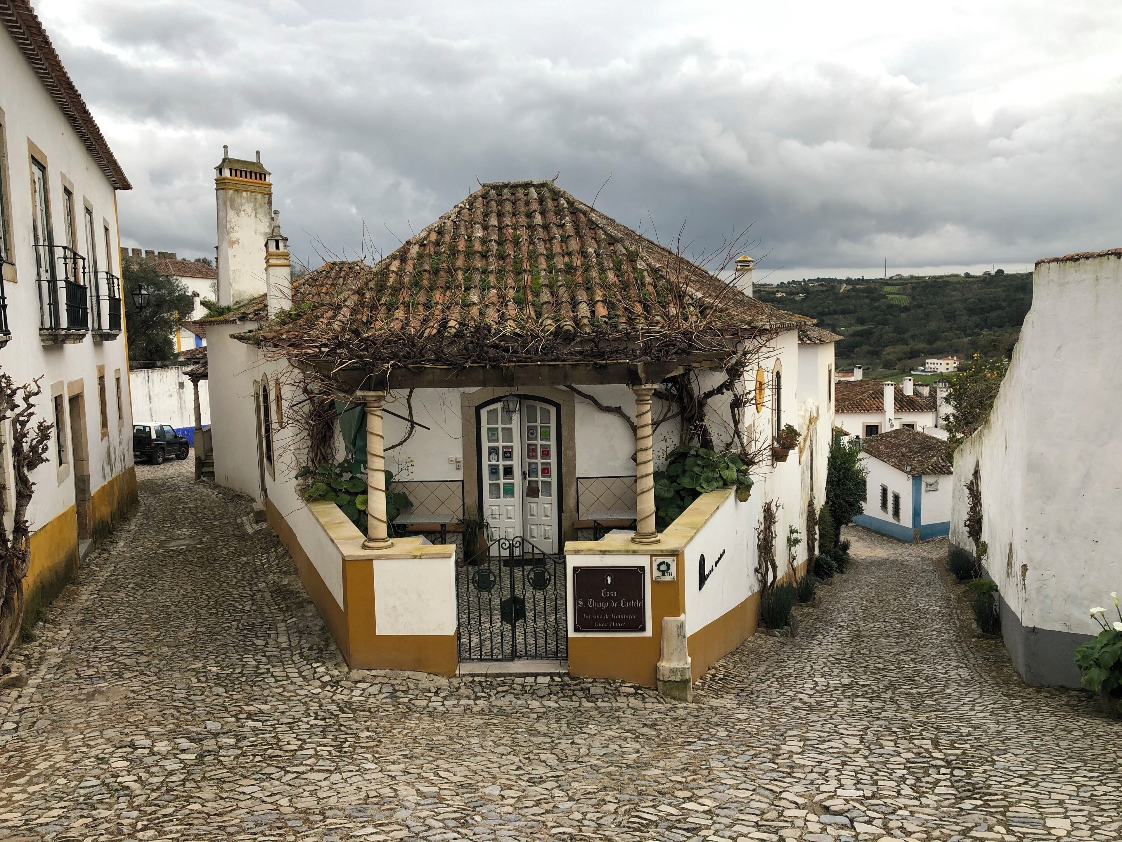 A narrow cobblestone street with a small building featuring a tiled roof and a white door.