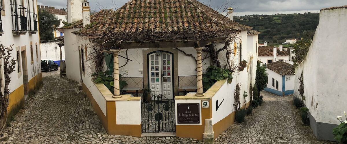 A narrow cobblestone street with a small building featuring a tiled roof and a white door.