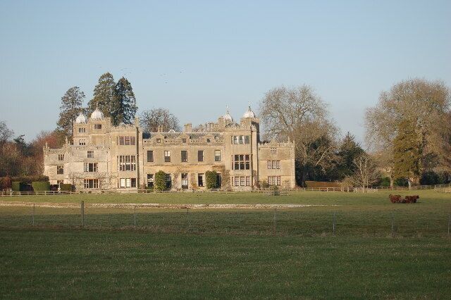 A large, historic stone building with multiple towers and a well-maintained lawn in front.