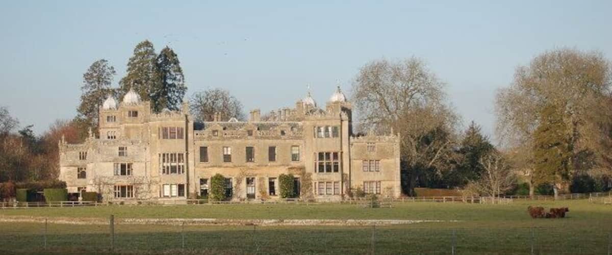 A large, historic stone building with multiple towers and a well-maintained lawn in front.
