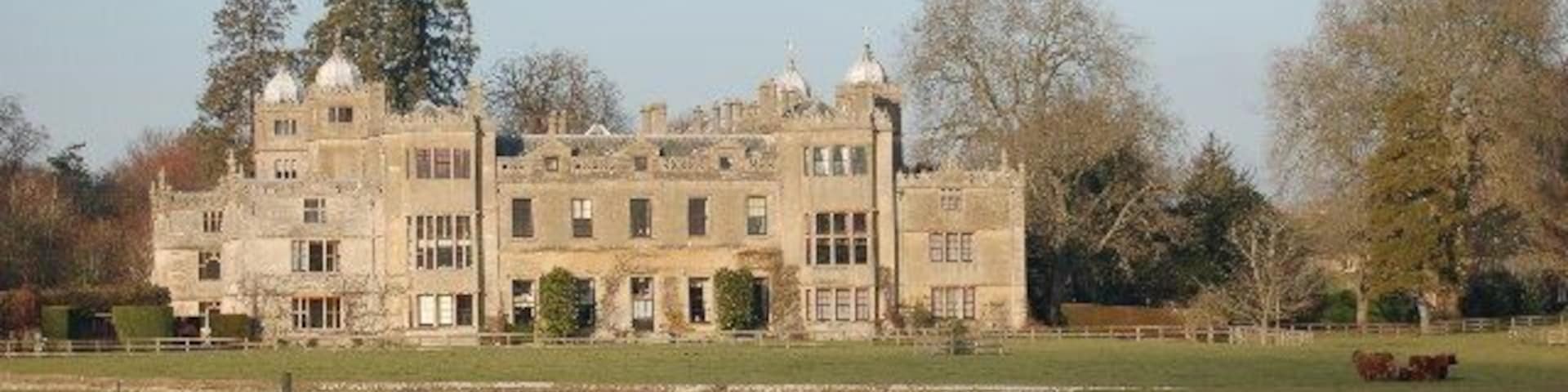 A large, historic stone building with multiple towers and a well-maintained lawn in front.