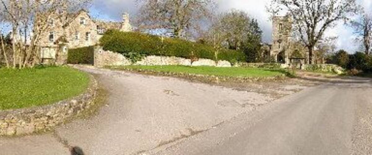 A rural road with stone walls and a large house in the background.