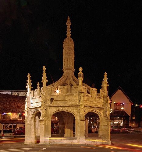 Un arco de piedra histórico con intrincados adornos y una alta aguja, iluminado durante la noche.