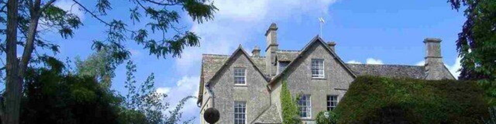 A large stone building with a traditional design, surrounded by well-maintained lawns and a stone wall.