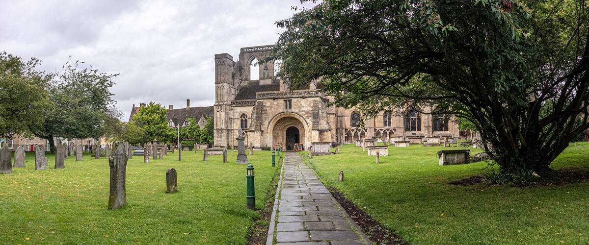 A historic church with a large arched entrance, surrounded by a cemetery with headstones and a pathway leading to the church.