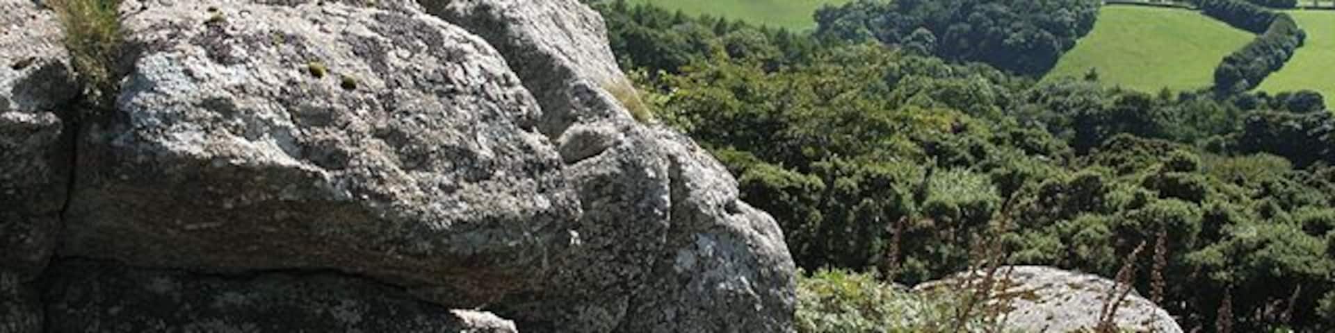 A rocky outcrop overlooking a green valley with fields and distant hills.