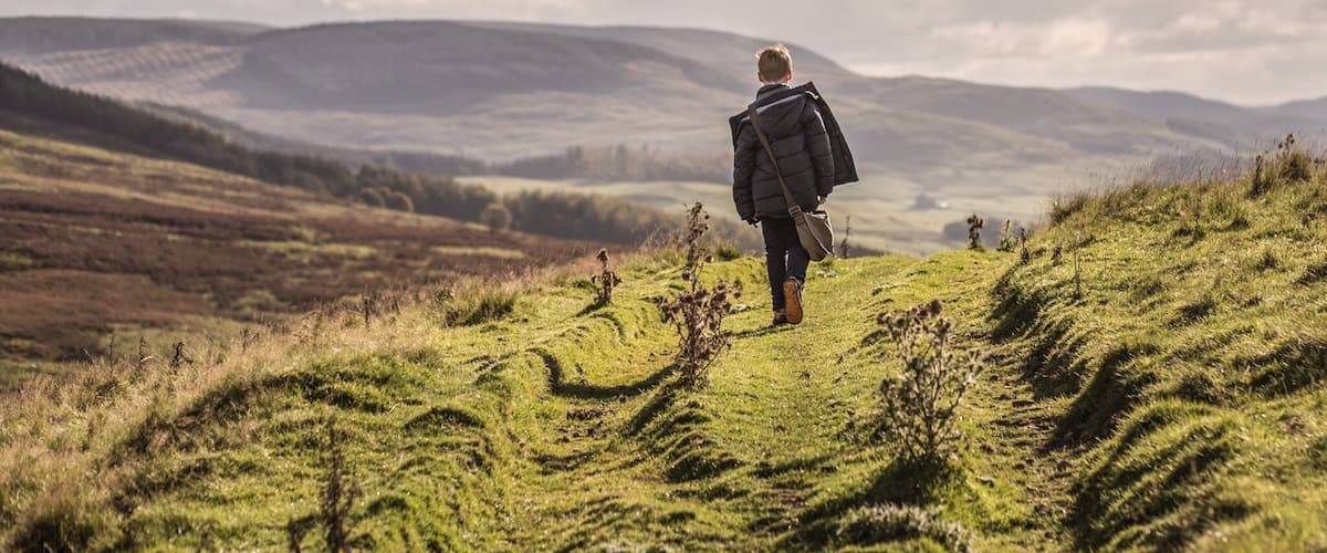A person walking on a grassy hill with rolling hills in the background.