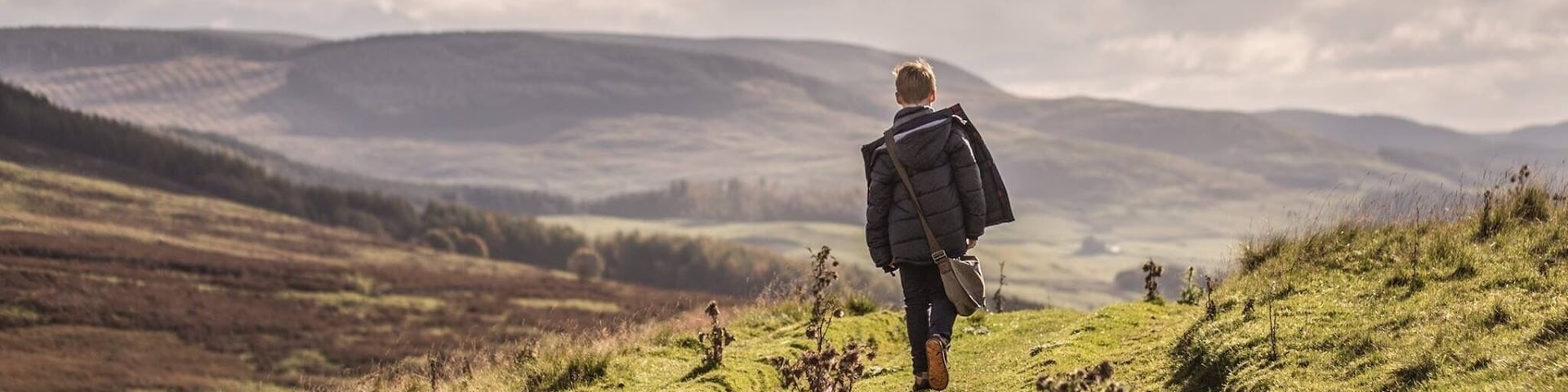 A person walking on a grassy hill with rolling hills in the background.