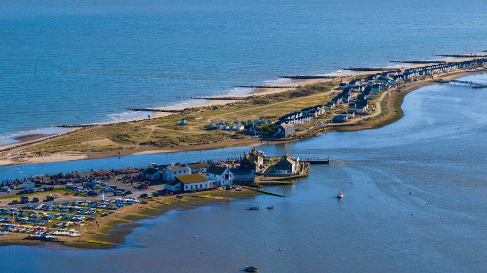 An aerial view of a coastal area with a marina, beach, and row of houses along the shore.